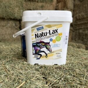 A white bucket of Natu-Lax horse supplement on hay.