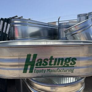 Metal water troughs stacked outdoors with Hastings logo.