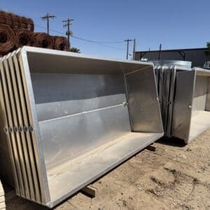 Several large metal bins stacked outdoors in a sunny, industrial setting.
