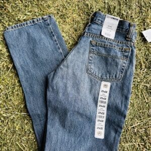 Pair of blue denim jeans with tags on green carpet.