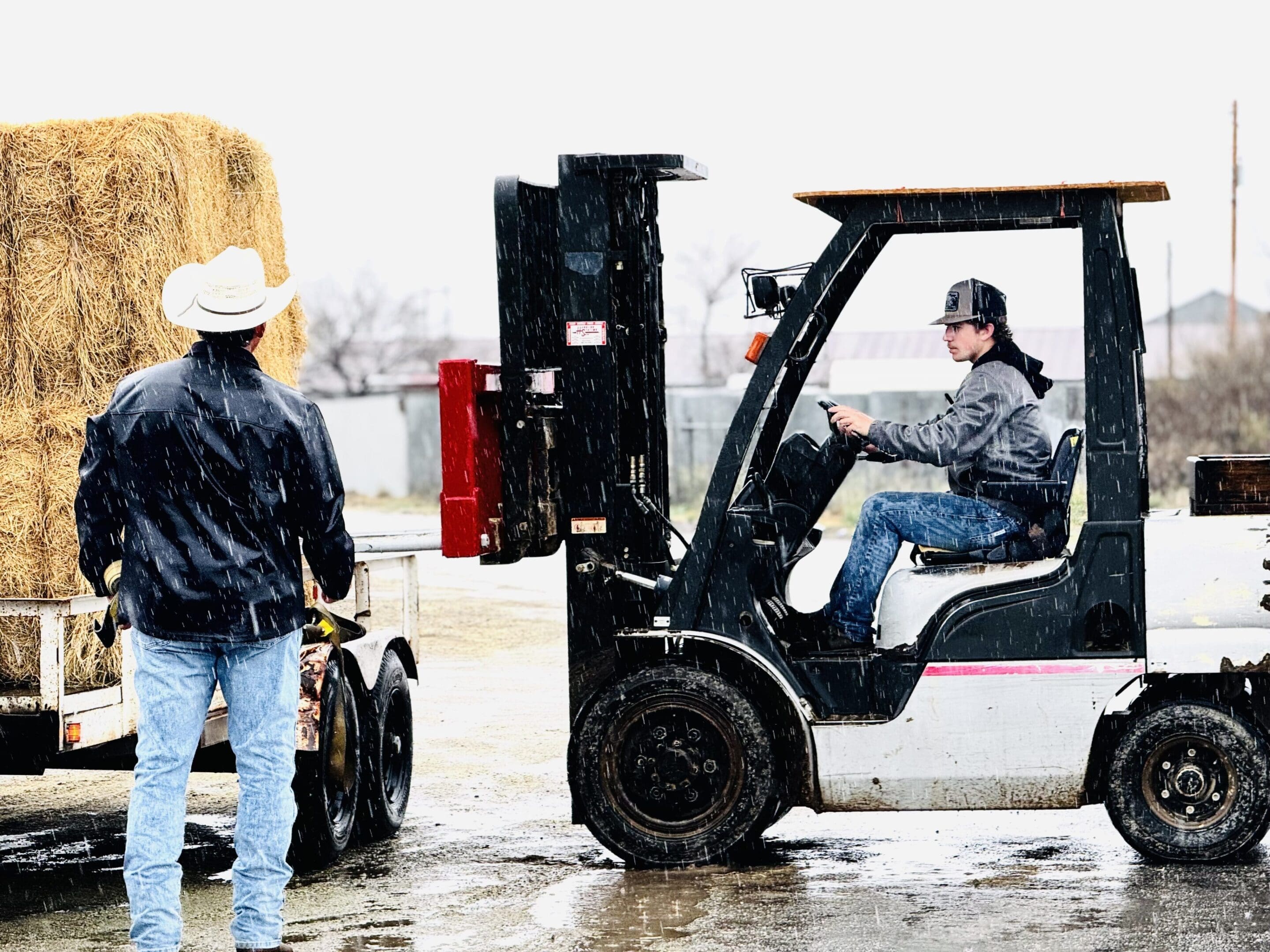 Two men working with forklifts in a snowy industrial area.