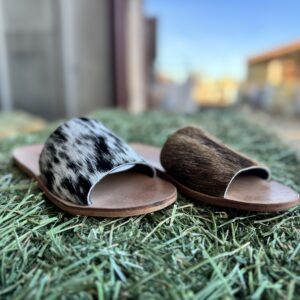 Two uniquely patterned slide sandals on grass.