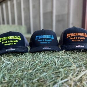 Three Stronghold Feed and Supply hats on hay