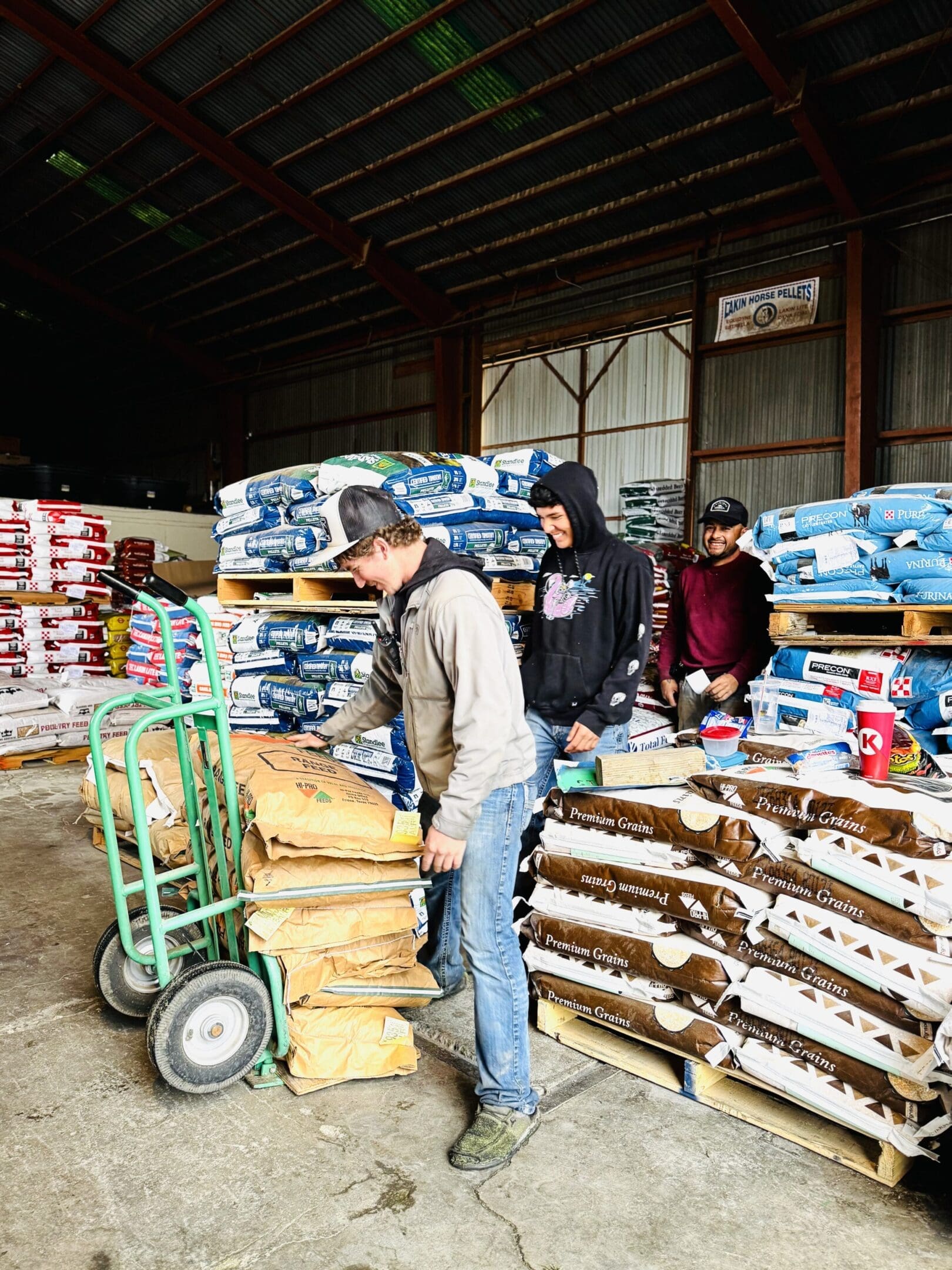 Three people working with large bags of pet food in a warehouse.